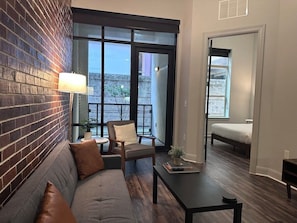 Ein modernes Wohnzimmer mit Backsteinwand, einer Couch, einem Sessel, einem Tisch und einem Balkon mit einem Bett.