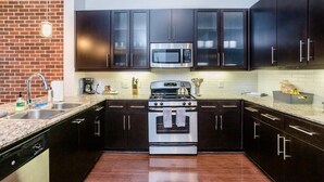 A modern kitchen with dark cabinets, stainless steel appliances, and a brick wall. - Rose at the Millennium - Stylish 1 BR in Houston (Houston)