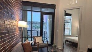 A modern living room with a brick wall, a sofa, a chair, a table, and a balcony with a bed. - Rose at the Millennium - Stylish 1 BR in Houston (Houston)