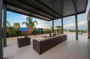 An outdoor patio area with seating, a TV screen, and a view of palm trees.