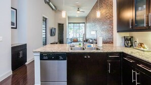 A modern kitchen with a dishwasher, dark cabinetry, a brick accent wall, and pendant lighting. - Rose at the Millennium - Stylish 1 BR in Houston (Houston)