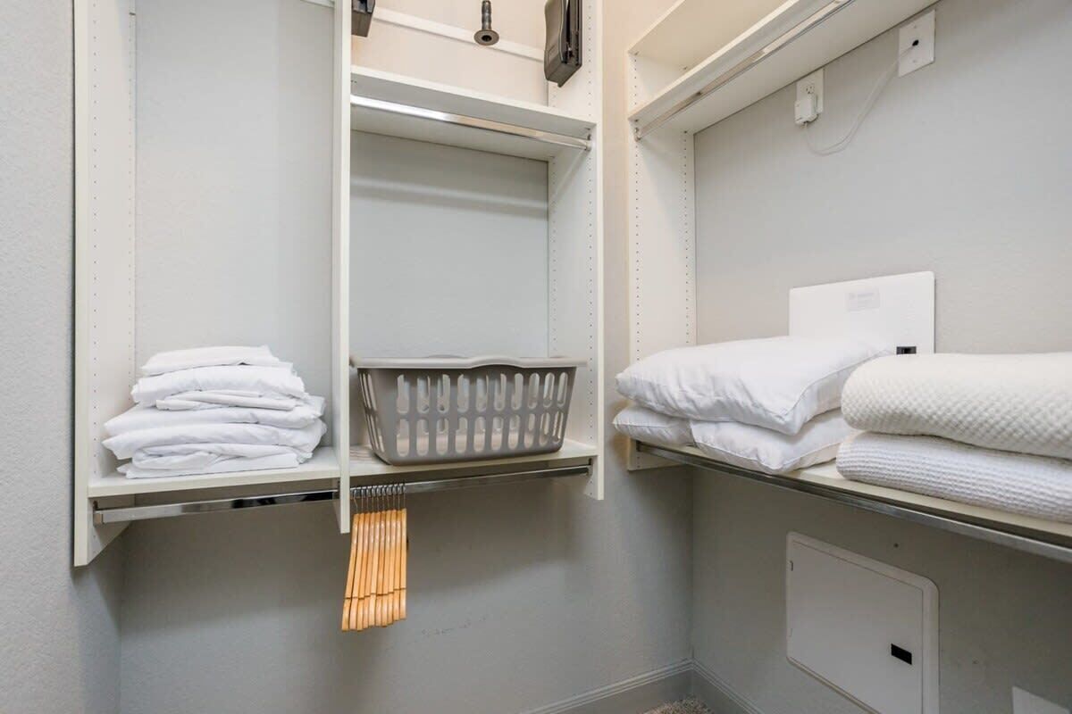 A bathroom with a white sink, a mirror, a towel rack, and a shelf with folded towels.