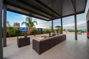 An outdoor patio area with a large sofa, a TV, and a dining table. - Jade At Millennium - 3 Bed Apt in Houston (Houston)