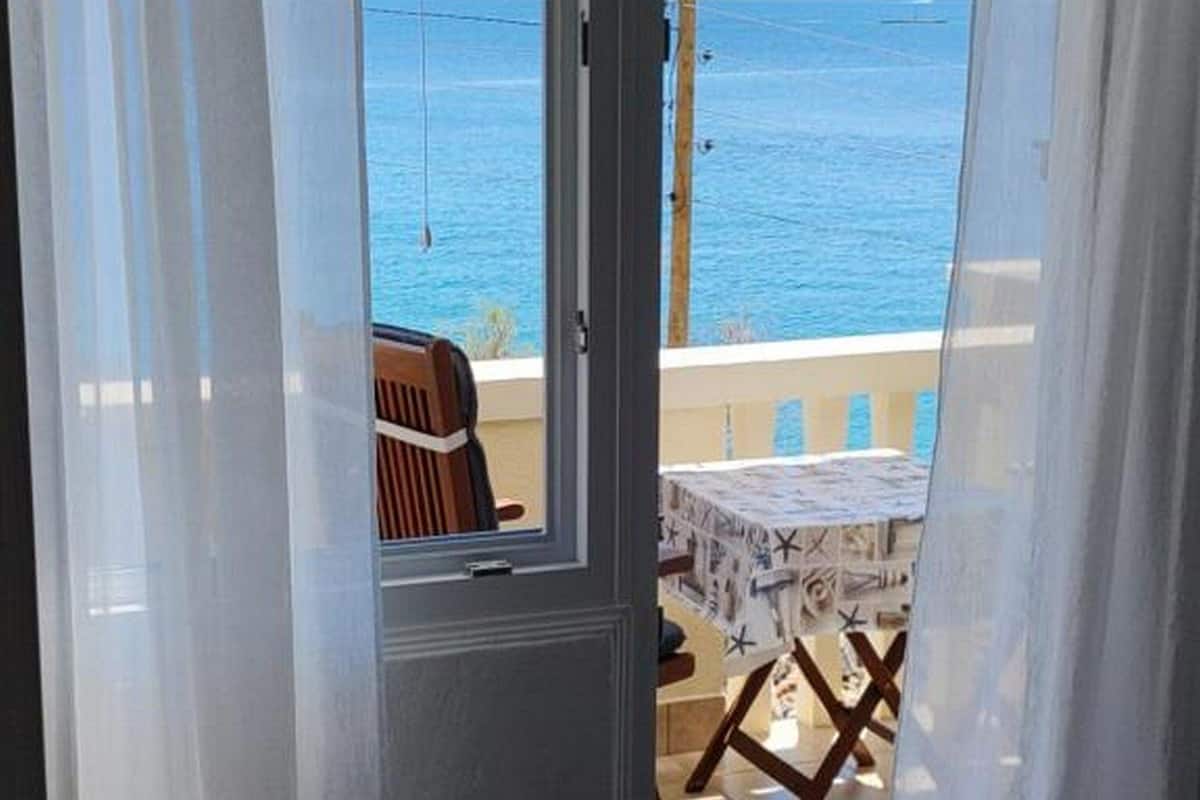 A room with a view of the sea through a glass door, a table with a tablecloth, and a chair.