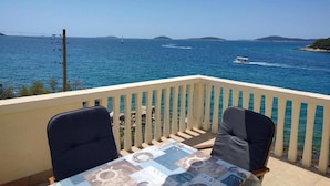 A balcony with two chairs and a table, overlooking a clear blue sea with boats and distant islands. - Apartments Blaža (Prvic Luka)