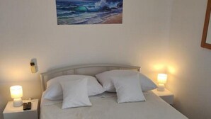 A neatly made bed with white linens and two rolled towels on the bed. There is a painting of a seascape on the wall above the bed. - Apartments Blaža (Prvic Luka)