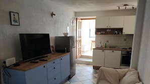A compact living space with a TV on a wooden cabinet, a kitchenette with cabinets and appliances, and a tiled floor. - Apartments Blaža (Prvic Luka)