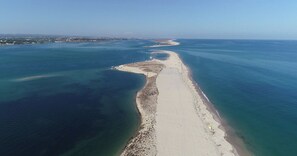 Vue aérienne d’une zone côtière avec une plage de sable et des eaux d’un bleu limpide.