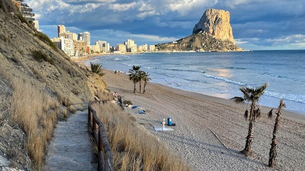 A coastal cityscape with a prominent rocky hill, a beach with palm trees, and a stone pathway leading to the beach. - High Quality Villa, 39 Five STAR REVIEWS, Beach 5 min drive, Heated Pool. (Calpe)