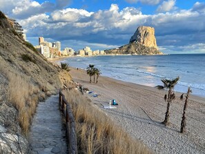 Eine Küstenstadt mit einem markanten Felsen, einem Strand mit Palmen und einem steinernen Weg, der zum Strand führt.