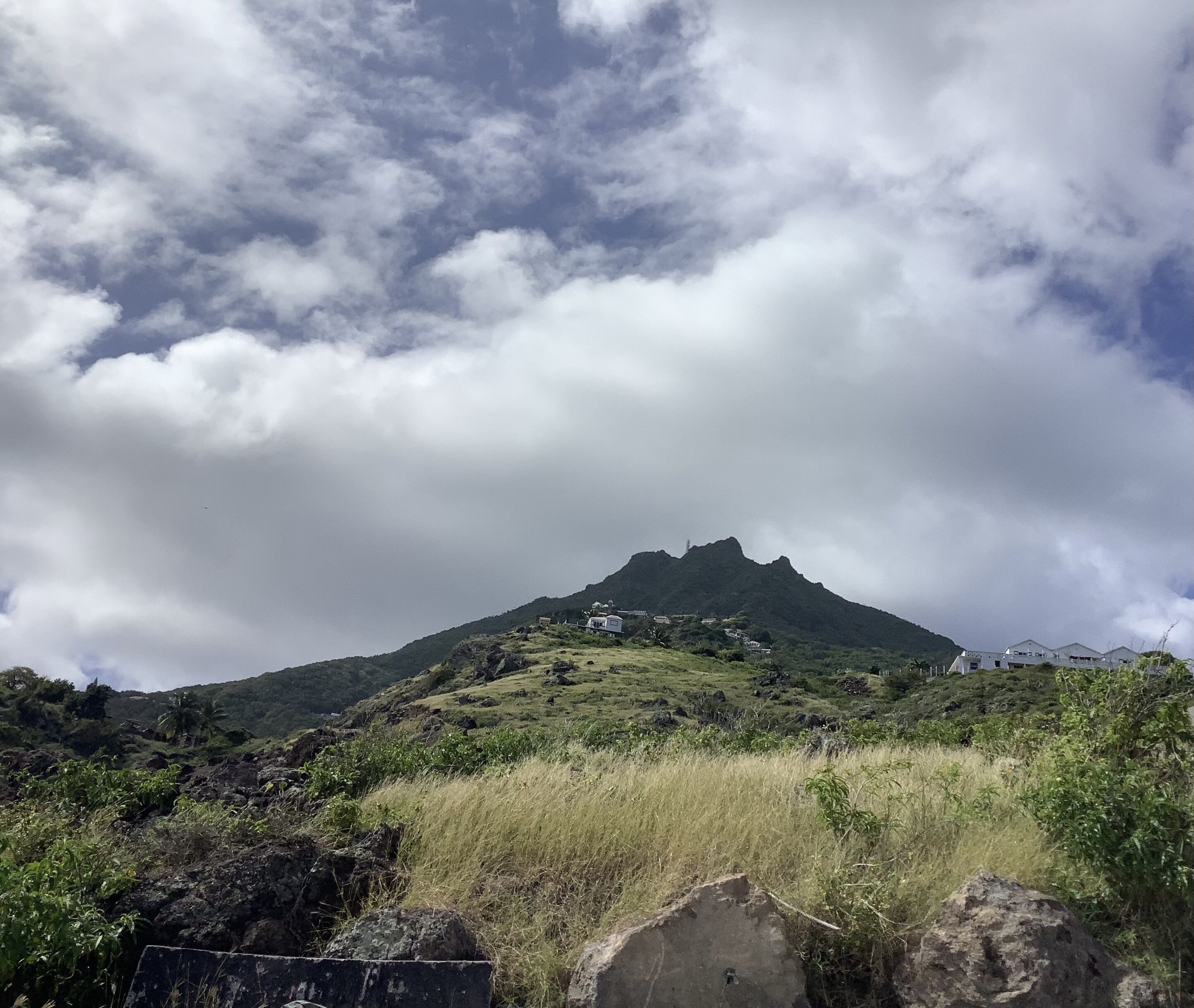 Una montaña con un primer plano cubierto de hierba y un cielo nublado.