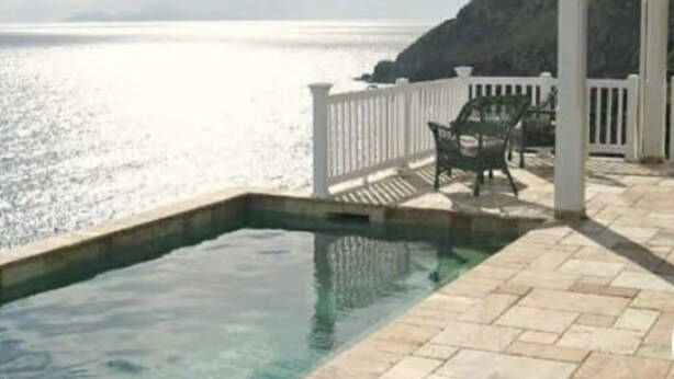 Una piscina con cerca blanca y sillas en un patio que da a un cuerpo de agua.