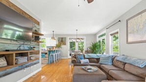 Un soggiorno ampio con una grande TV, scaffali in legno, un divano marrone e un'area pranzo con sedie e tavolo.