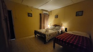Une chambre avec deux lits, une fenêtre avec des rideaux, un ventilateur de plafond et un climatiseur fixé au mur.