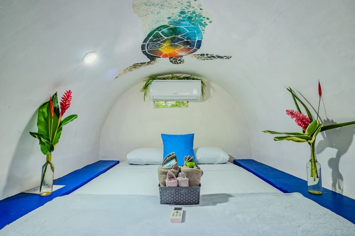 Een kamer met een bed, een klein tafeltje met handdoeken, en twee vazen met planten.