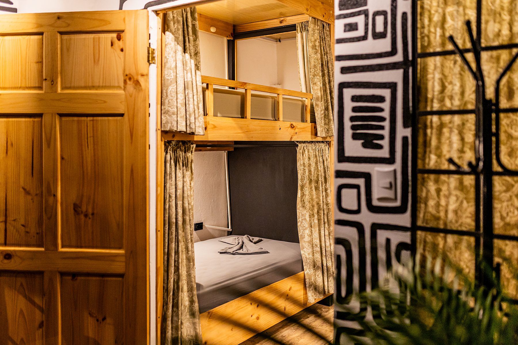 A bunk bed with a wooden frame and curtains, a small window, and a patterned wall.