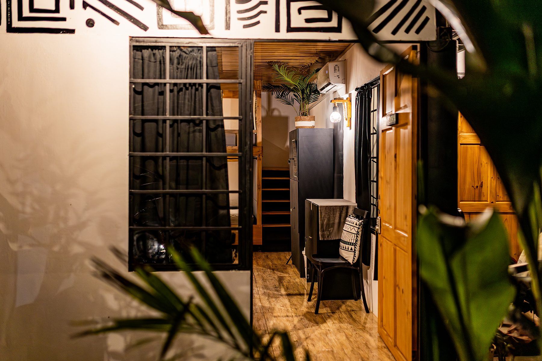 A narrow hallway with a wooden floor, a metal-framed window, and a door leading to a room.