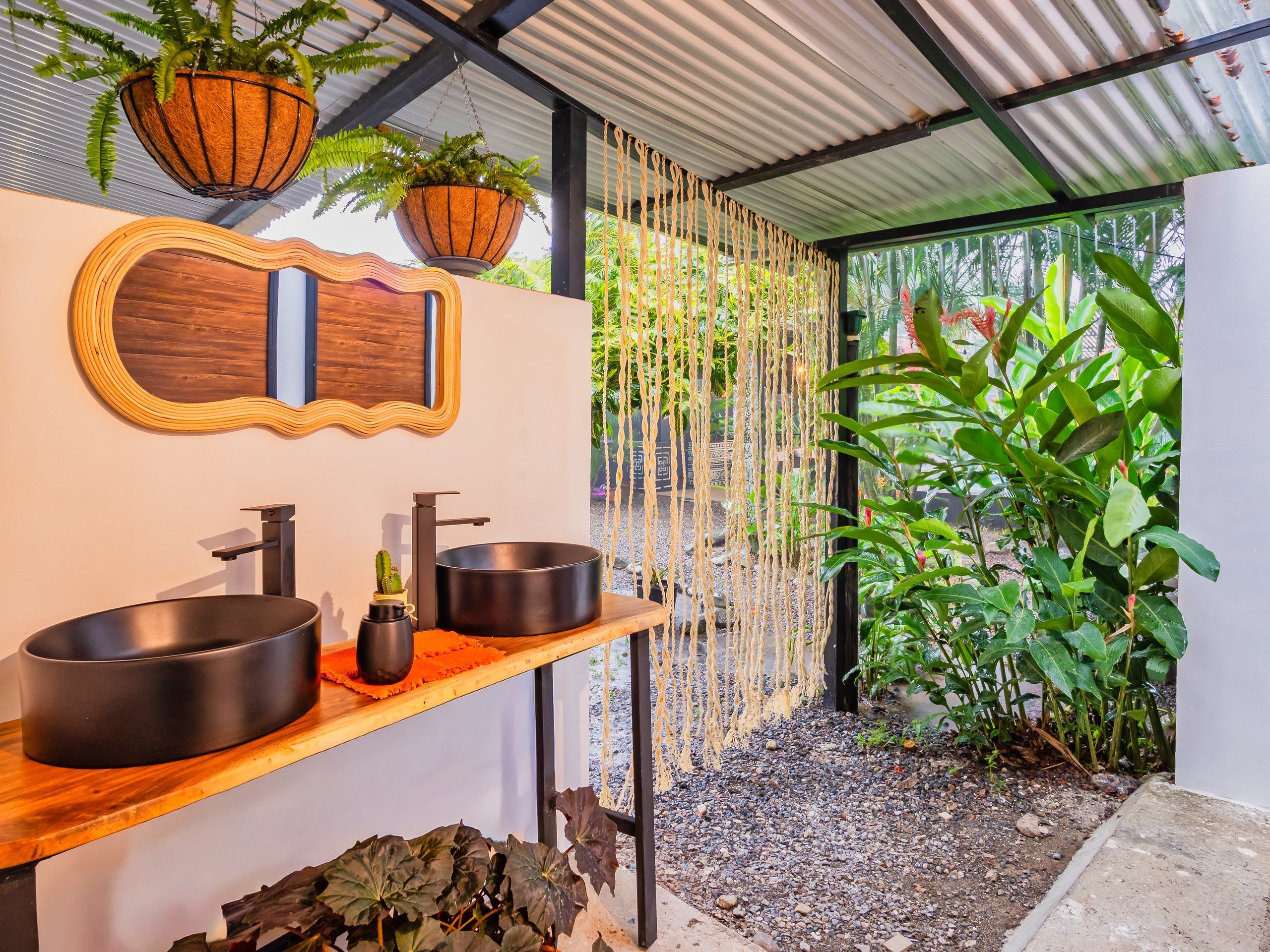 A modern bathroom with a wooden vanity, two black sinks, a mirror, and hanging plants.