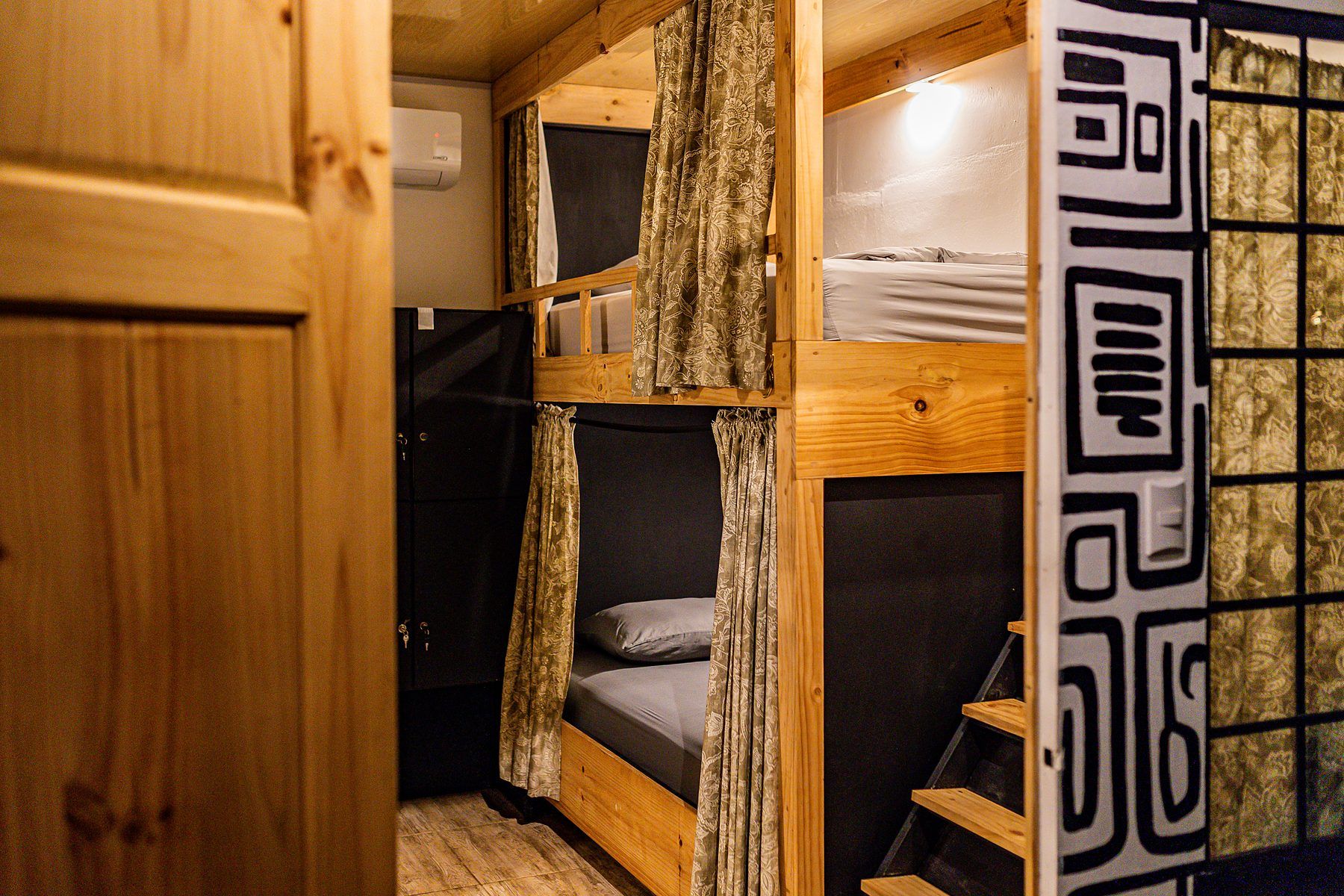 A bunk bed room with a wooden ladder, a small closet, and a patterned curtain.
