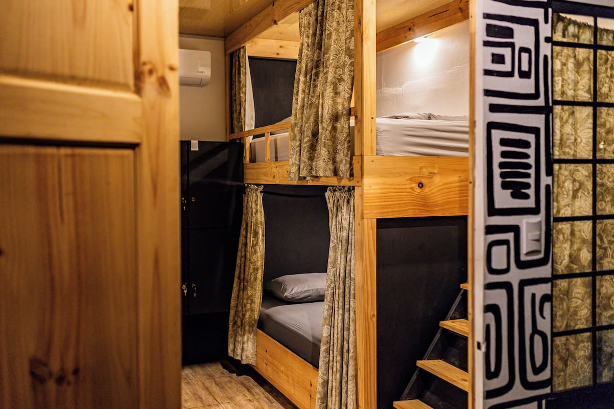 Een slaapkamer met stapelbedden, houten wanden, een klein bureau en een gordijn.