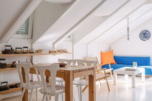 Un salón-comedor amplio y luminoso con una mesa y sillas de madera, un sofá azul y una lámpara colgante.