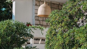 En stentrappe fører op til en hvid dør med et gittermønster, omgivet af frodig vegetation og en hængende lampe.