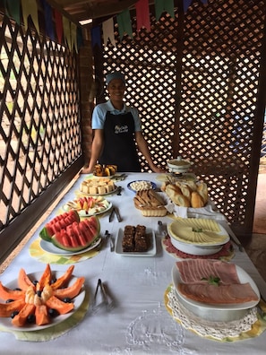 Mesa de buffet com diversos alimentos e uma pessoa atrás dela.