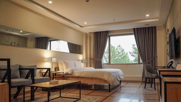A modern hotel room with a large bed, a sofa, a desk, and a TV. - Roomy Signature Hotel (Islamabad)