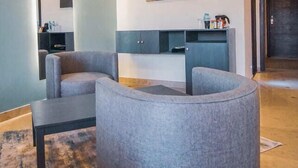 A modern living room with a grey sofa, a small coffee table, and a wall-mounted TV. There is a painting above the TV and a dark-colored cabinet below it. - Roomy Signature Hotel (Islamabad)