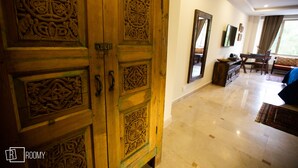 A room with a wooden door with intricate carvings, a flat-screen TV mounted on the wall, a sofa, and a dining table with chairs. - Roomy Signature Hotel (Islamabad)