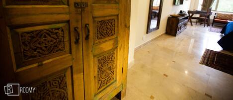 A room with a wooden door with intricate carvings, a flat-screen TV mounted on the wall, a sofa, and a dining table with chairs.