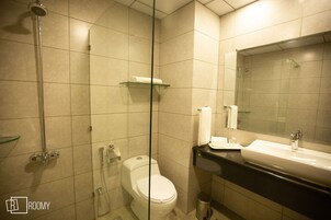 Un baño con ducha de vidrio, inodoro, lavamanos con espejo y repisa sobre el inodoro.