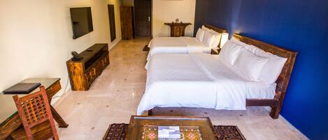 A hotel room with two beds, a desk, a chair, a coffee table, and a TV mounted on the wall.