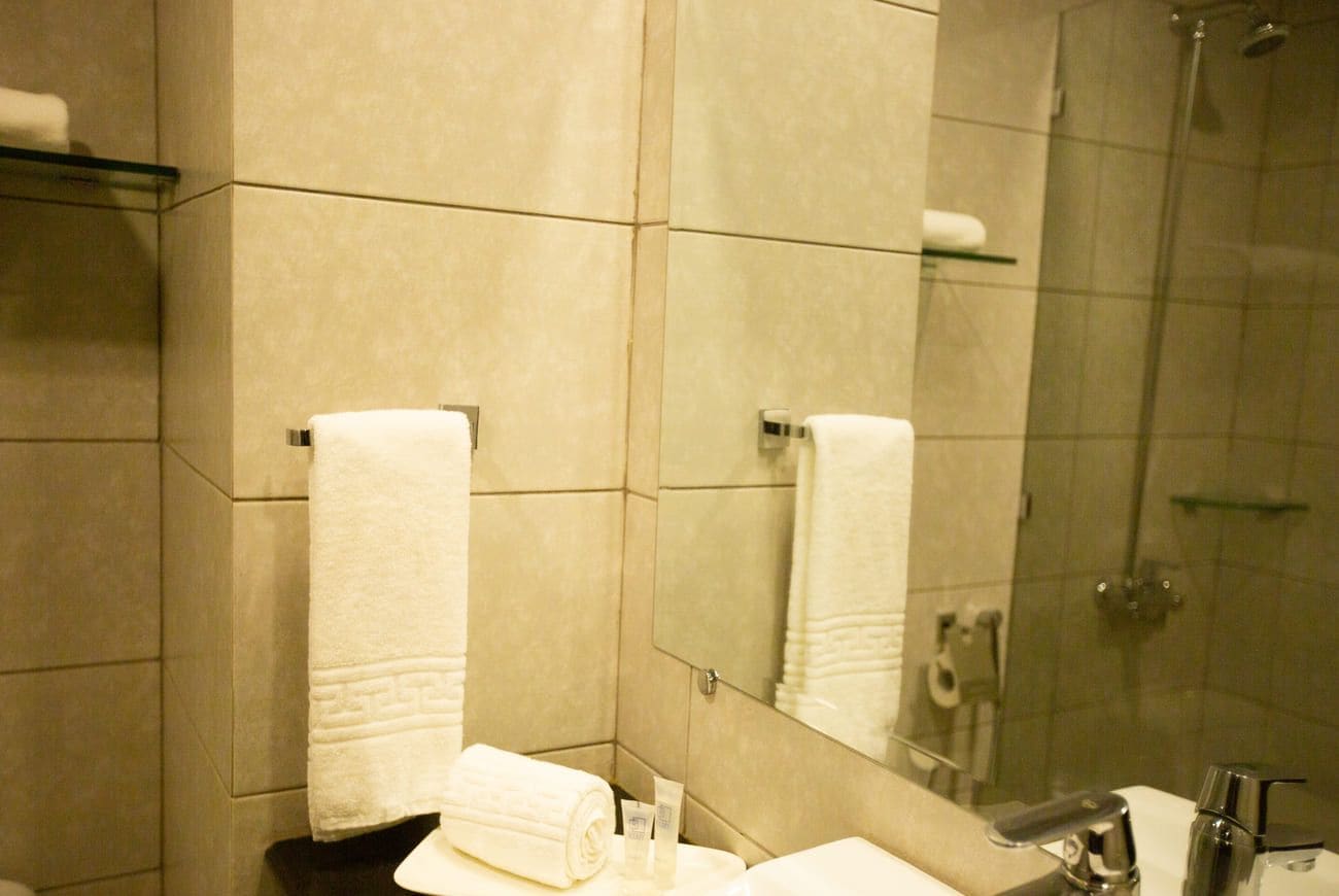 A bathroom with a sink, mirror, and shower. There are towels and toiletries on the counter.