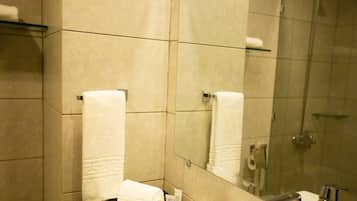 A bathroom with a sink, mirror, and shower. There are towels and toiletries on the counter.