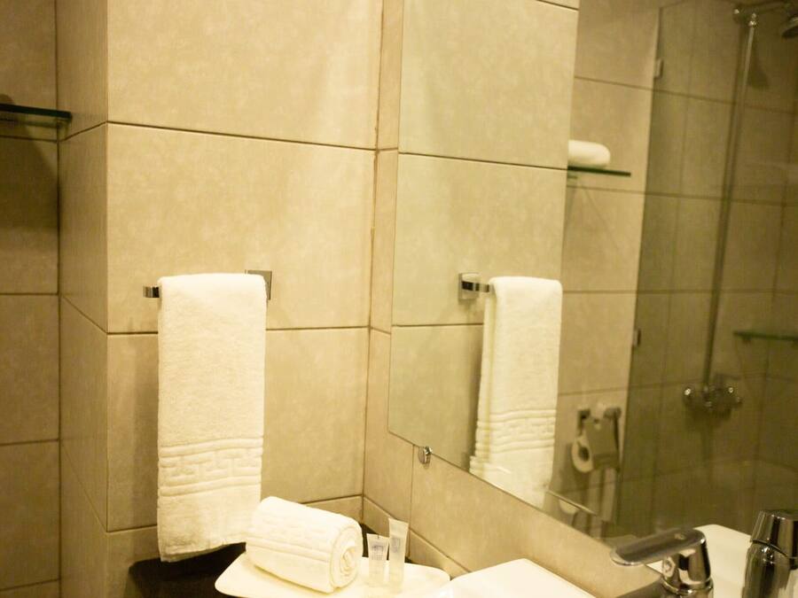 A bathroom with a sink, mirror, and shower. There are towels and toiletries on the counter.