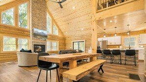 Ein großzügiges Blockhaus-Interieur mit einem großen Esstisch, verschiedenen Sitzmöglichkeiten, einem Kamin und einer Küchenzeile.