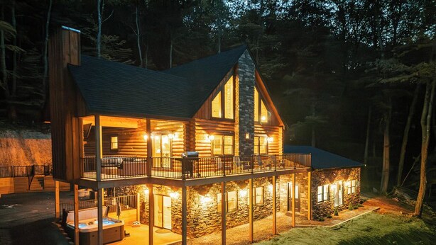 Eine Blockhütte mit Balkon, Whirlpool und Naturstein-Fassade.