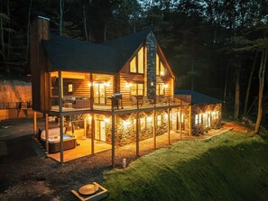 A log cabin with a balcony, a hot tub, and a stone exterior.