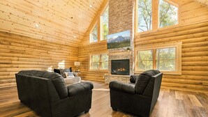 Ein rustikales Blockhaus-Interieur mit Kamin, zwei schwarzen Ledersofas und großen Fenstern.