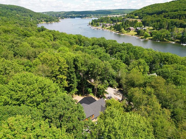 A secluded cabin surrounded by dense forest, overlooking a lake with boats and a small dock.