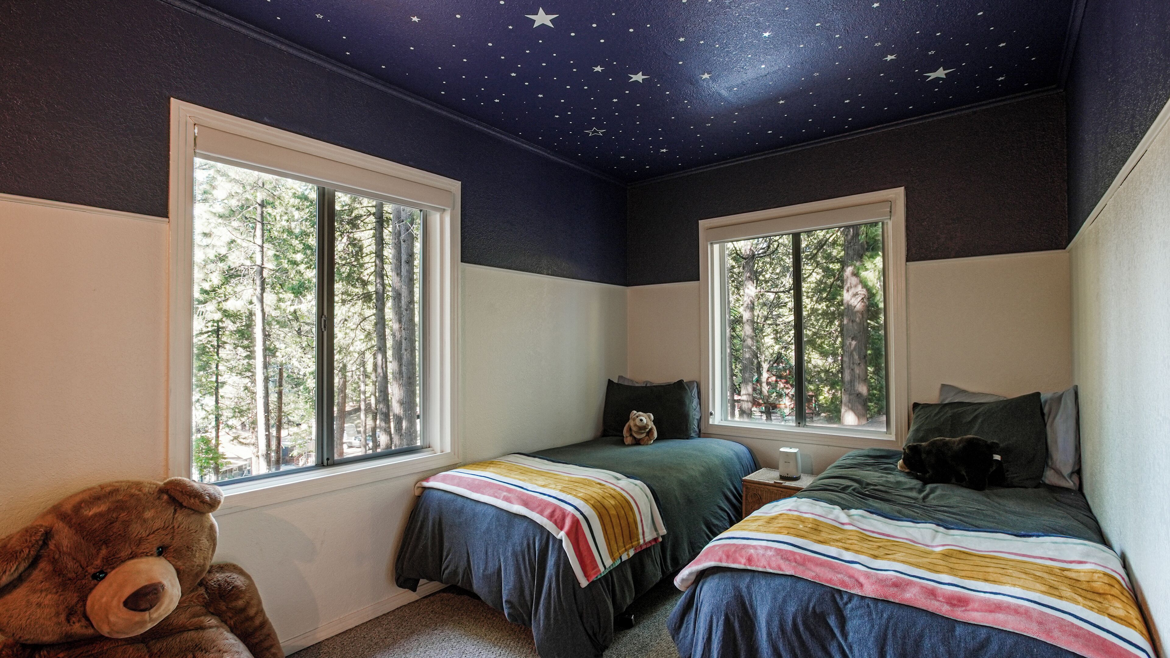 Un dormitorio con dos camas, un oso de peluche grande y techo estampado con estrellas.