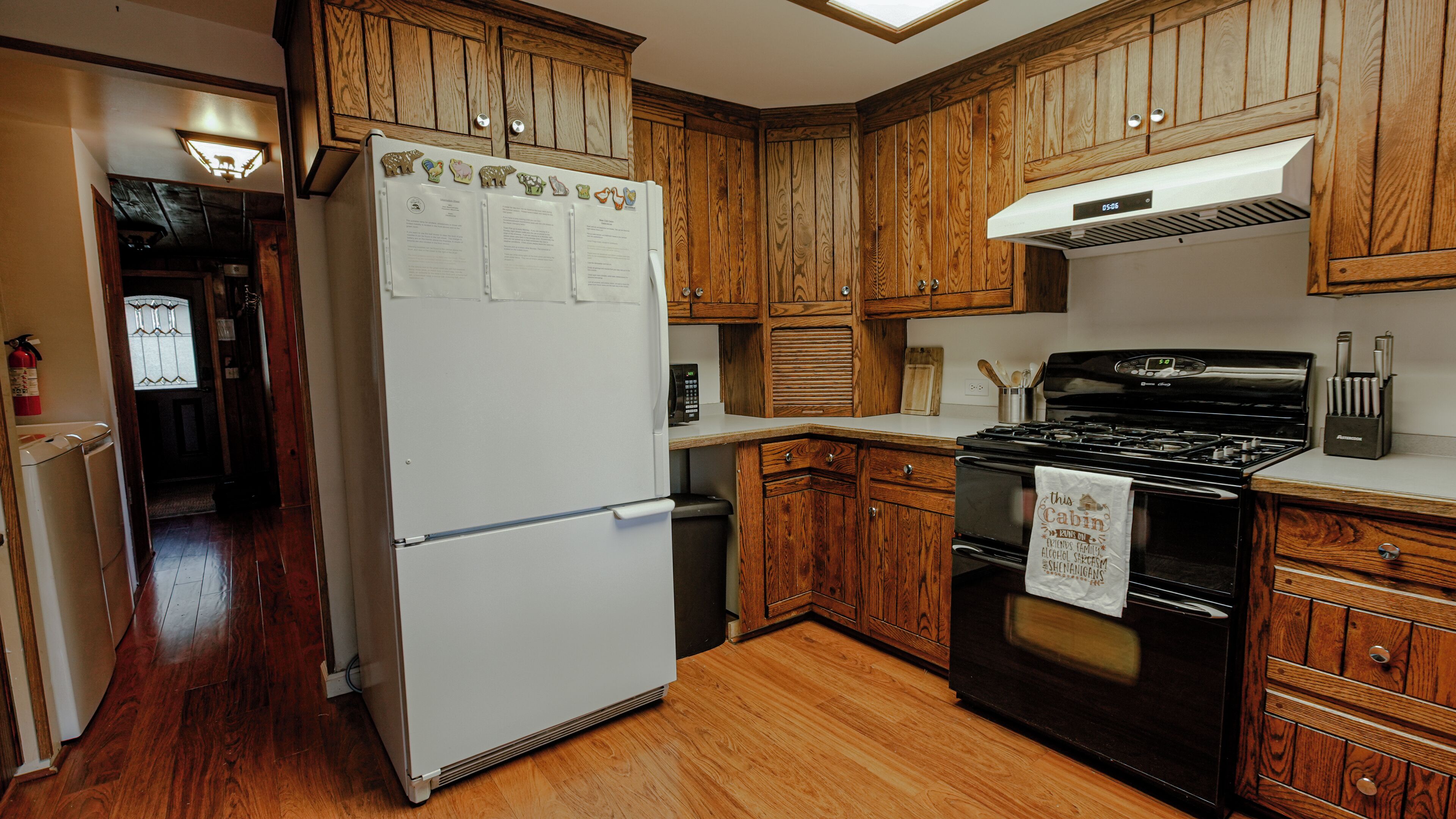 Une cuisine avec des meubles de rangement en bois, un réfrigérateur blanc, une cuisinière noire et un plancher en bois.