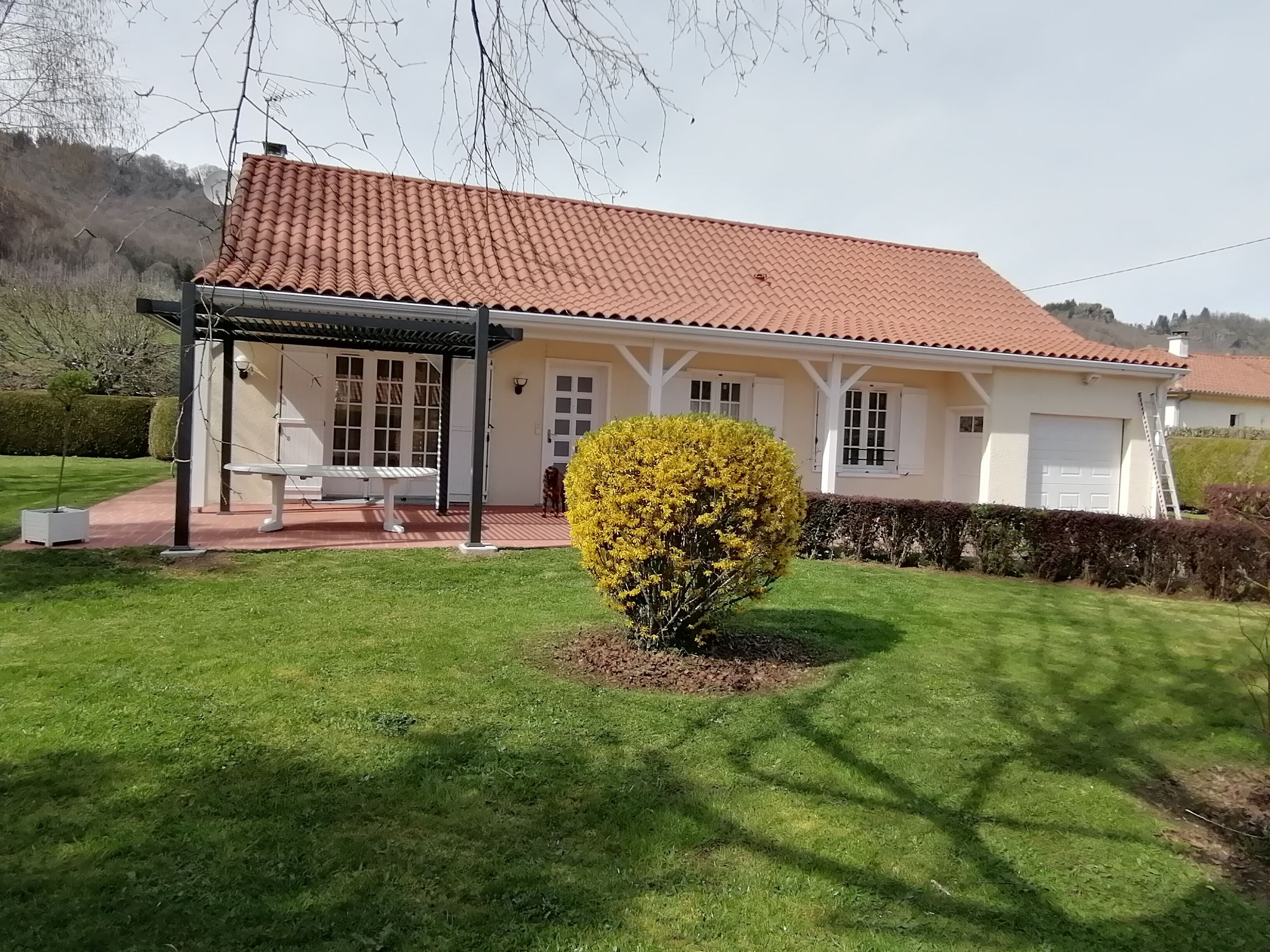 A white house with a red-tiled roof, a covered patio, and a well-maintained lawn.