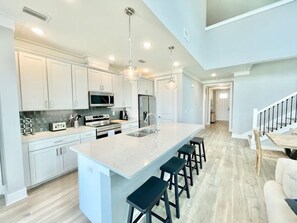 A modern kitchen with white cabinets, a large island with bar stools, stainless steel appliances, and pendant lighting. - Newly Constructed Beautiful Coastal Style Home Lake Powell Panama City Beach (Panama City Beach)