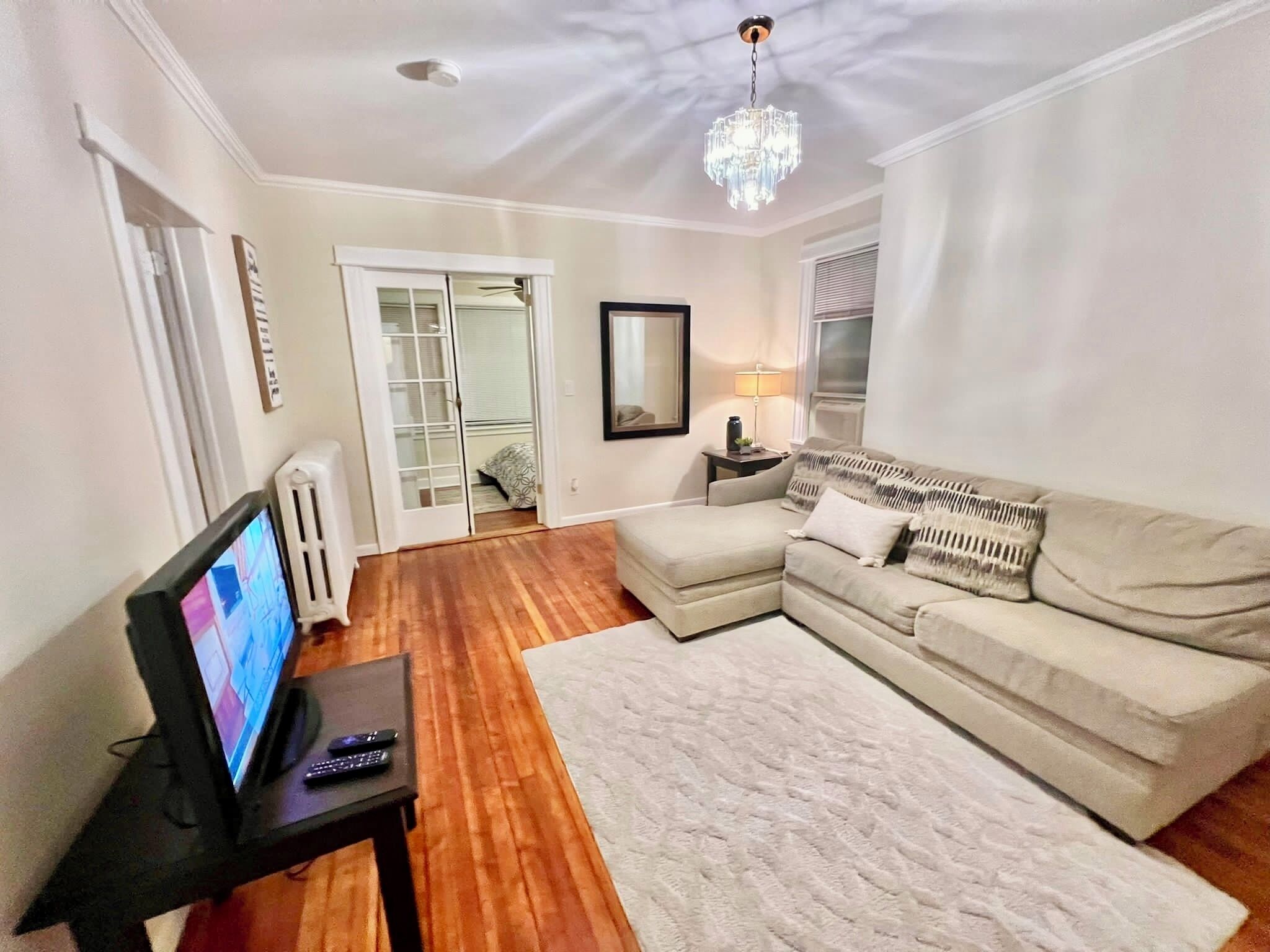 A living room with a sofa, a television, a coffee table, and a chandelier.