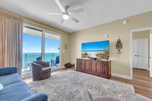 Relax in this stylish living room with a large flat-screen TV, sliding glass door to a balcony with ocean views, and a cozy armchair.