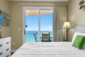 Relax in this serene retreat with a large bed, wooden dresser, and dining table, offering a peaceful ocean view from the balcony.