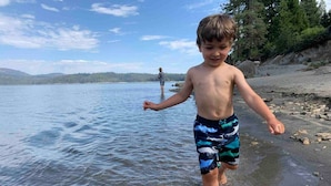 A child walking on a beach with a calm lake and a forest in the background.