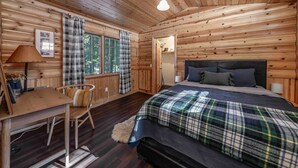 A wooden cabin bedroom with a bed, a desk, and a chair.